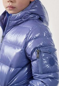 Chaqueta acolchada morada con acabado brillante, bolsillo con cremallera en la manga y capucha. Presenta secciones acolchadas y un logotipo circular en el brazo.
