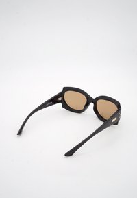 Μαύρα ορθογώνια γυαλιά ηλίου με καφέ φακούς και φαρδιές πλάγιες βάσεις, τοποθετημένα σε λευκή επιφάνεια, από την πίσω και πλευρική όψη.