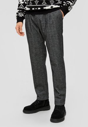 Grijze gemêleerde broek met plooien en zijzakken, gecombineerd met zwarte enkellaarsjes. De trui heeft een geometrisch zwart-wit patroon.
