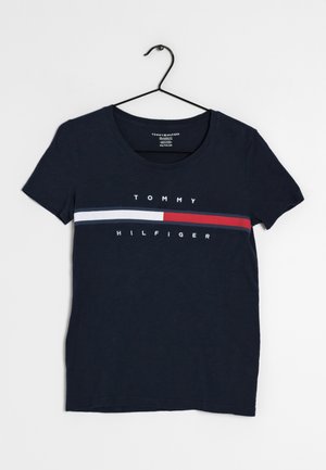 T-shirt Tommy Hilfiger bleu marine avec des rayures horizontales rouges, blanches et bleues et le nom de la marque, suspendu à un cintre noir.
