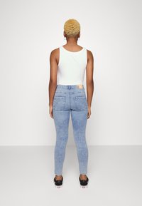 Chino skinny jeans em denim azul claro apresentam uma cintura alta, bolsos traseiros e uma textura levemente desbotada. Combinados com uma t-shirt branca.