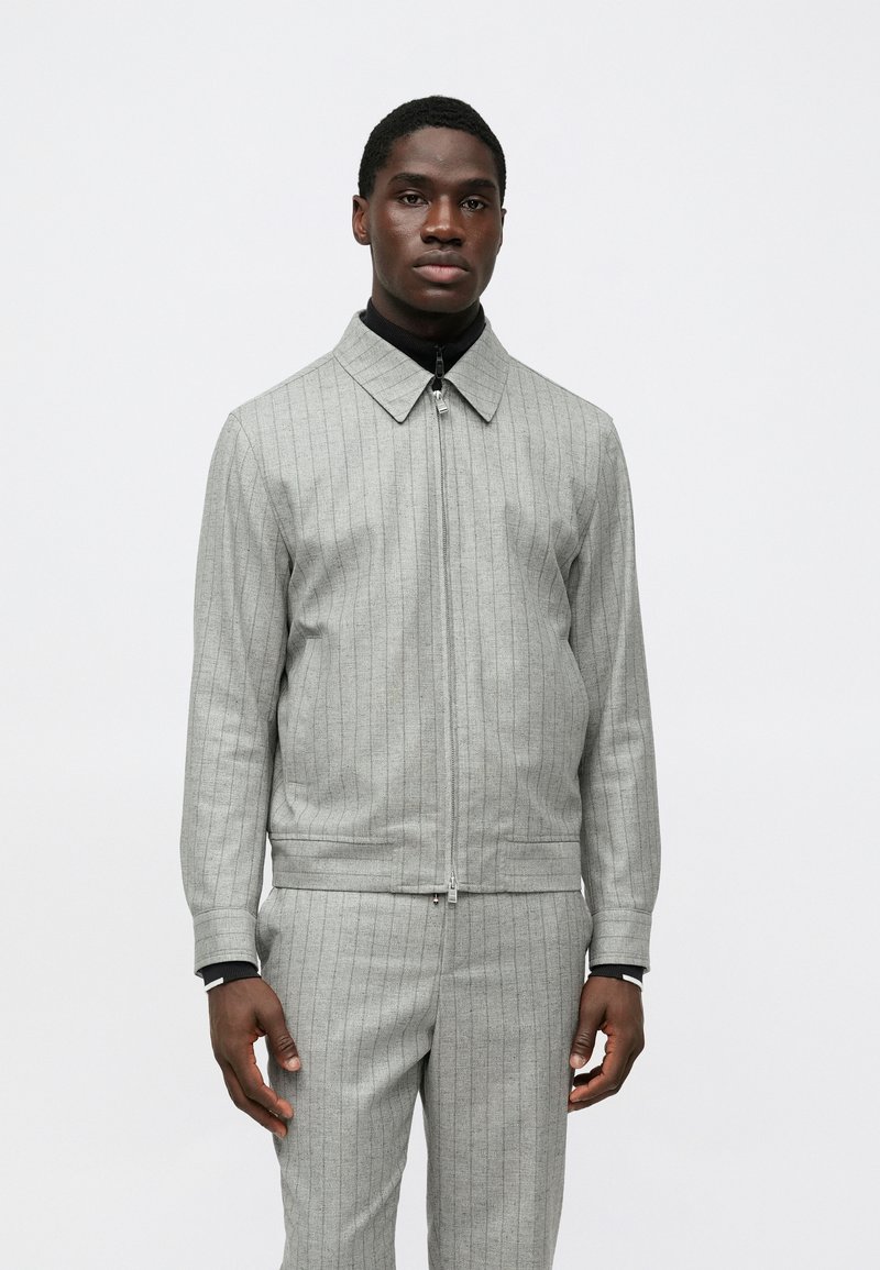 Γκρι μπλελοφόρο μπουφάν με στενές λωρίδες, κλείσιμο με φερμουάρ και γιακά. Κατασκευασμένο από υφή υφάσματος. Λεπτή γραμμή, σετ με ταιριαστό παντελόνι.