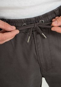 Pantalones de color gris oscuro con un ajuste relajado, que cuentan con una cinturilla elástica y cordón ajustable. Ojetes metálicos y cordón trenzado como detalle de sujeción.
