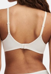 Cremefarbener BH aus glattem, elastischem Stoff. Verstellbare Träger und Verschluss hinten, mit einem abgerundeten Rückendesign und minimalen Akzenten.