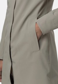 Cappotto impermeabile grigio chiaro con tasca laterale, design elegante e texture liscia, che enfatizza funzionalità e stile minimalista.
