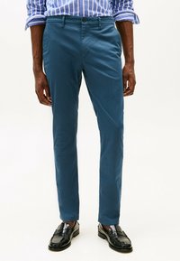 Pantaloni slim-fit in teal realizzati in un tessuto misto cotone; presentano tasche anteriori e una texture sottile. Abbinati a mocassini neri.
