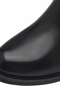 Gros plan sur le bout d'une chaussure en cuir lisse noir avec des coutures visibles et une forme carrée arrondie.