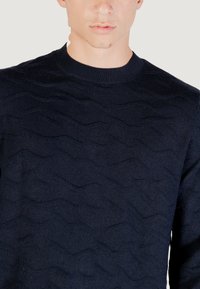 Maritimer, gestrickter Pullover mit einem strukturierten Wellenmuster, Rundhalsausschnitt und gerippten Bündchen. Aus weichem Stoff gefertigt, der dezente Details zeigt.