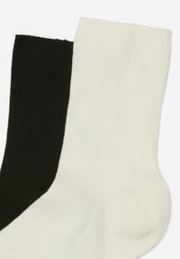 Bawełniane skarpetki w czerni i bieli, z kądzielnym wzorem. Czarna skarpetka znajduje się po lewej, a biała po prawej.