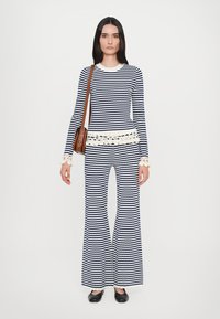 Bluză tricotată cu dungi bleumarin și alb, cu tiv ondulat, asortată cu pantaloni evazați. Include o geantă de umăr maro și pantofi negri.