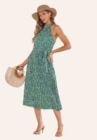 Abito midi verde senza maniche con collo all'americana, pois bianchi e cravatta in vita. La modella tiene una borsa di paglia ed indossa sandali con cinturini marroni.