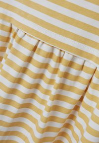 Gelb- und weiß gestreifter Stoff mit einem rüschierten Saum. Die Streifen sind gleichmäßig verteilt, mit einer glatten Textur. Die Nähte sind sauber verarbeitet.