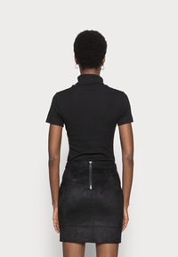 Un col roulé noir à manches courtes côtelé associé à une mini-jupe en daim noir avec une fermeture éclair au dos, une texture lisse et une coupe ajustée.