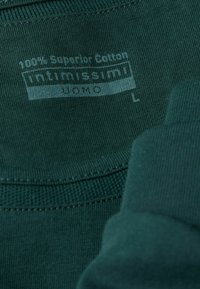Dunkelgrünes Baumwoll-T-Shirt mit einem Etikett, auf dem "100 % Superior Cotton" und "intimissimi UOMO" steht, Größe L. Glatte Textur mit geripptem Ausschnitt.