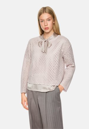 Helles rosa Oberteil mit einem strukturierten, offenen Strickdesign, einem satinartigen Kragen und passender Schleife. Kombiniert mit grauen gestreiften Hosen.