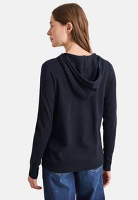 Marineblauer Hoodie aus weichem Stoff mit Kordelzug, gerippten Bündchen und Saum. Verfügt über ein kontrastierendes Innenfutter, das am Rand der Kapuze sichtbar ist.