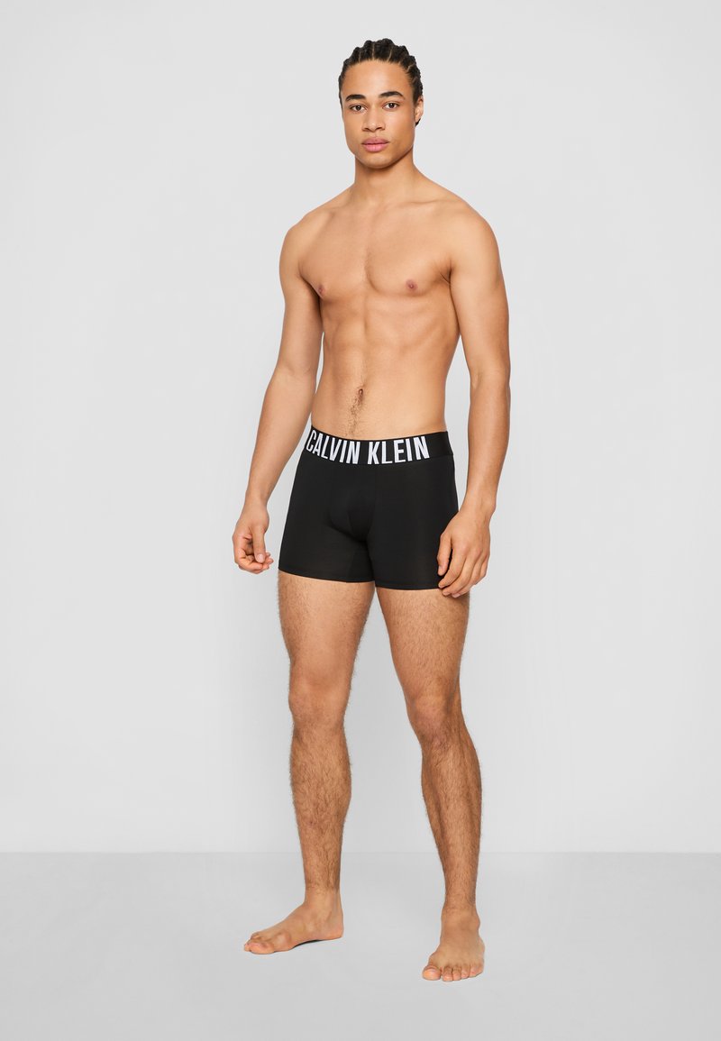 Black boxer briefs with white "Calvin Klein" logo on the waistband, featuring a fitted design and smooth fabric texture.