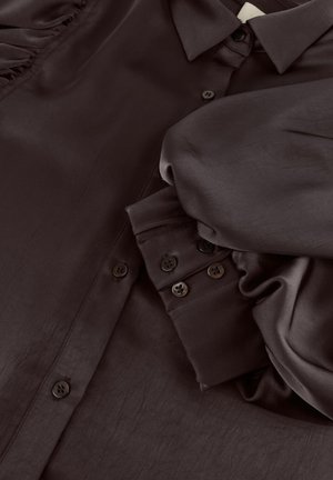 Donkerbruine satijnen blouse met opgeblazen mouwen, knoopmanchetten en een puntige kraag, plat gelegd.