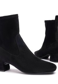 Stivali alla caviglia in suede nero con tacco basso e punta affilata, mostrati su uno sfondo bianco.