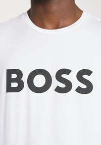 Vit bomull t-shirt med fet svart "BOSS"-tryck. Rund halsringning, korta ärmar, mjuk textur, minimalistisk design.