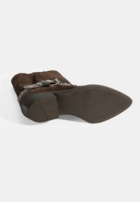 Braune Wildleder-Ankle-Boots mit niedrigem Blockabsatz, versehen mit einem gürtelförmigen Akzent und silbernem Beschlag sowie einer strukturierten Gummisohle.