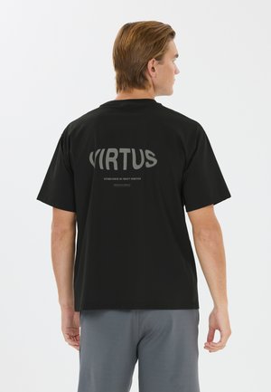 Mand med lysebrunt hår iført en sort t-shirt med teksten "VIRTUS" på ryggen, kombineret med grå bukser, med fronten væk fra kameraet.