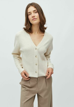 Cardigan crema a coste con scollo a V profondo, con sei bottoni frontali e polsini aderenti, abbinato a pantaloni marroni su misura.