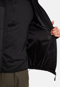 Sort yderjakke med kviltet tekstur; indvendigt foret med glat sort stof. Lynlåslukning og justerbar kant. Casual design.