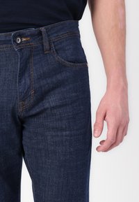 Donkerblauwe denim jeans met een soepele textuur, voorzien van een klassiek vijf-pocket ontwerp, subtiele stiksels en een metalen knoopsluiting.