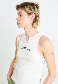 Débardeur blanc à côtes avec un col en forme de trou de serrure, arborant un logo noir "DICKIES". Tissu léger avec un design ajusté.