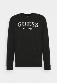 Sudadera negra de algodón, con cuello redondo, mangas largas y un destacado texto en blanco "GUESS EST. 1981" en la parte frontal.