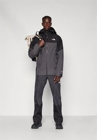 Mustast ja hallist veekindlast kapuutsiga jopest, luku ja logoga. Koos sobivate pükste ja mustade tossudega. Seljas rihmaga seljakott üle õla.