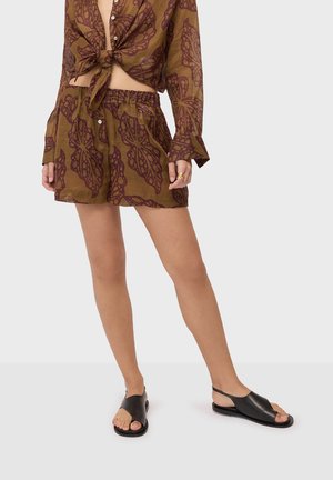 Ensemble marron deux pièces avec motifs abstraits de feuilles violettes, haut à manches longues noué, short assorti à taille élastique, et sandales noires à talon slingback ouvertes à l\'avant.
