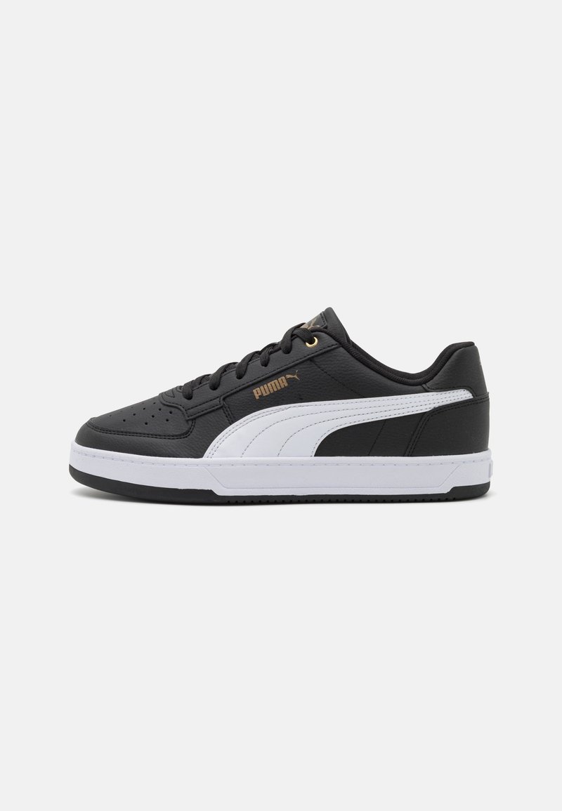 Baskets en cuir noir Puma avec bande latérale blanche, lacets noirs, logo Puma doré et semelle blanche sur fond gris clair.