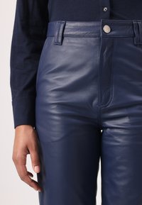 Pantalons en cuir marine au toucher lisse, avec fermeture éclair et bouton à l'avant, passants de ceinture et coupe ajustée à la taille.