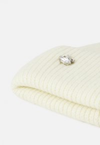 Tessuto knit color crema a costine con bordo ripiegato, caratterizzato da una spilla in tonalità argento con pietre trasparenti sulla superficie.