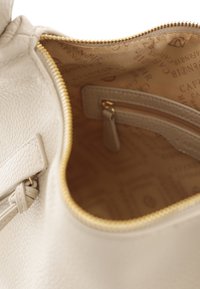 Krémová kožená taška má interiér s uzavíráním na zip, hladkou texturou a světle hnědým vzorovaným podšívkou se zipovou kapsou.