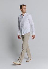 Witte linnen overhemd met een staande kraag, beige broek en lichte sneakers. De outfit heeft een ontspannen pasvorm en een minimalistisch ontwerp.
