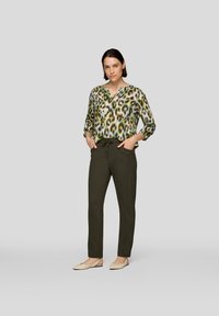Kurzärmlige Bluse in einem grünen und cremefarbenen, abstrakten Tiermotiv, kombiniert mit olivgrünen Hosen und beigen Ballerinas.