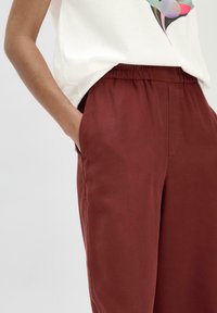 Bordeauxrode broek met een elastische waistband, zijzakken en een gladde textuur. Gecombineerd met een lichtkleurige graphic t-shirt.