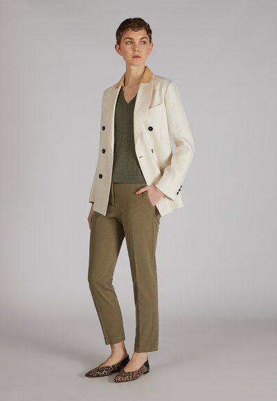 Blazer de lino crema con botones negros sobre una blusa de pico verde oliva y pantalones oliva. Unos zapatos planos de estampado de leopardo completan el conjunto.