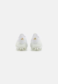 Zapatillas blancas con una textura suave, que presentan una suela translúcida y un acento dorado. La vista trasera muestra un diseño elegante y el logo de la marca.