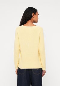 Sárga bordázott kötött pulóver kerek nyakkivágással és hosszú ujjakkal, laza szabással és puha tapintással, sötétkék, bő szárú farmernadrággal párosítva.