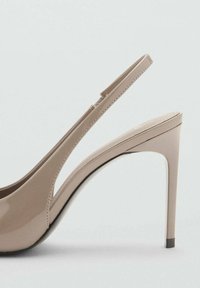 Nude patent leather high-heeled sandal with an open back, slingback strap, and a tapered heel. Smooth texture and minimalist design.