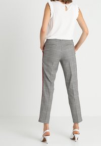 Pantalons gris à carreaux avec des rayures latérales rouges, conçus avec une coupe ajustée. Caractéristiques d'un tissu lisse et d'une longueur de cheville raccourcie.