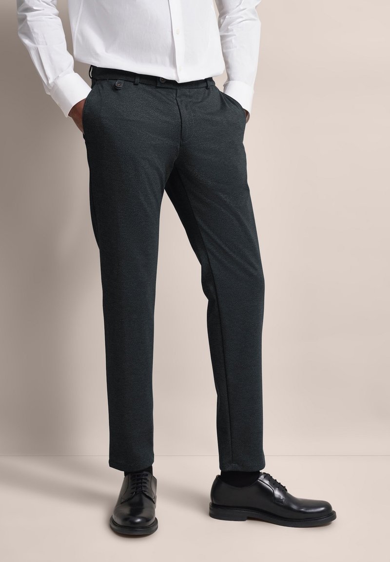 Dunkelgraue Hosen aus einem strukturierten Stoff, mit einer maßgeschneiderten Passform und Seitentaschen, kombiniert mit schwarzen Schuhen.