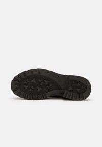 Suela de bota de goma negra con un patrón de dibujo profundo que presenta corazones y triángulos, destacando un material duradero y una superficie texturada para el agarre.