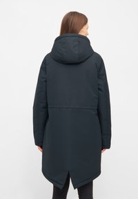 Svart vadderad jacka med huva, med en lätt rundad nederkant och textil med struktur. Visad från baksidan, med minimal designer detalj.