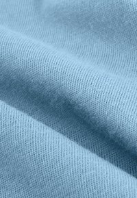 Helles blau gestricktes Gewebe mit einer glatten Textur. Es zeigt feine, gleichmäßige Rippungen, die ein weiches und geschmeidiges Erscheinungsbild erzeugen. Eine subtile Flauschigkeit ist sichtbar.