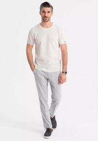 Camisa de punto blanca de manga corta con cuello redondo, acompañada de pantalones ajustados gris claro y zapatos oscuros con diseño de cordones.